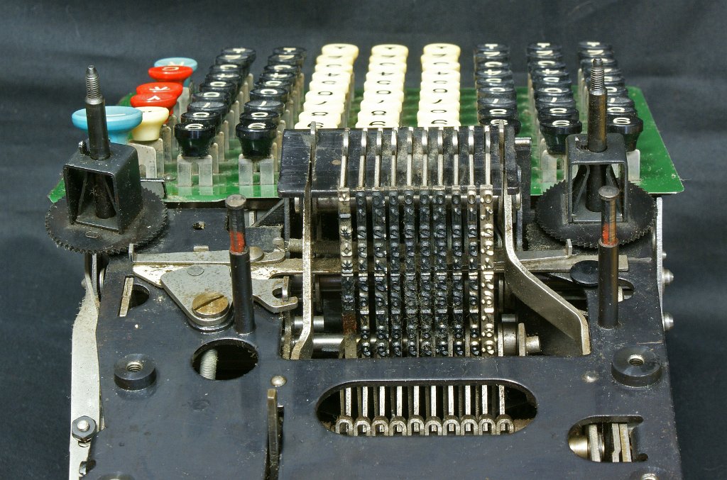 DSC07797.JPG - Close-up view on the 10 vertical number rods; the left-most holds the different symbols (like -,# etc.); the blank right-most rod seems not to have functioned very often. The machine is based on the rack and pinion ("Zahnstange", "crémaillère") mechanism: when for instance 5 is keyed in as the first digit, the second rod raises up so that the embossed 5 is in front of the ink ribbon, and a horizontal movement pushes the rod against the ribbon. and the paper.