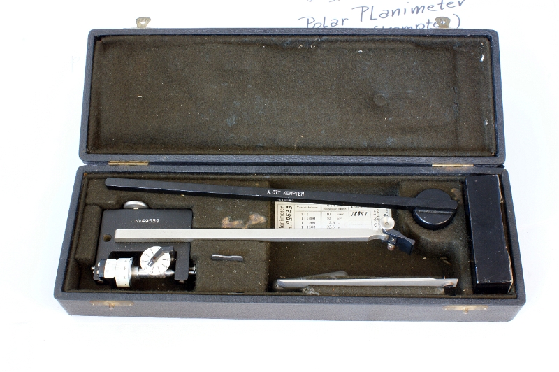 DSC04532.JPG - Box with the planimeter, the calibration bar and the heavy prismatic foot which has an opening to receive the cylinder at the right end of the first arm.